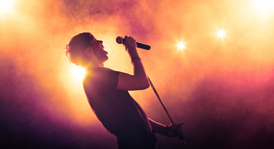 Young male singer with a microphone performing on stage in backlit