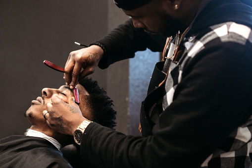 An African American man gets his hair cut by a skilled stylist at a small business barbershop.