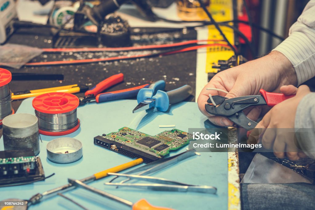 Close up of cutting wire with pliers in engineering laboratory. Close up of kid and his teacher using pliers and cutting wire while repairing something in tech laboratory. Adult Stock Photo