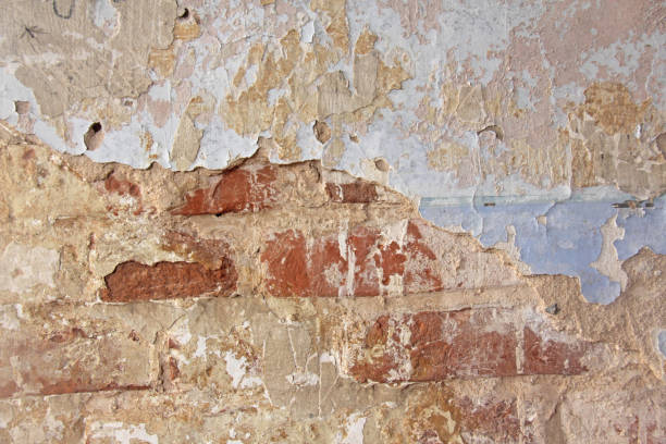 istock Old flaky white paint peeling off a grungy cracked wall. Cracks, scrapes, peeling old paint and plaster on background of old cement wall. An old cement stone wall as vintage cracked. Brick wall. 938770546