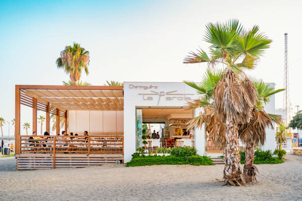 People sit at the patio of a chiringuito located at Malagueta beach in Malaga, Andalusia, Spain. Chiringuitos are usually small restaurant bars located on beaches.