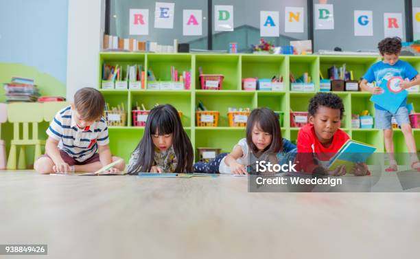 Photo libre de droit de Groupe Denfant De La Diversité Sétends Sur Plancher Et Lecture Livre De Conte À La Bibliothèque Dâge Préscolaire Concept Déducation École Maternelle banque d'images et plus d'images libres de droit de Enfant