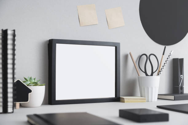 istock Creative desk with blank picture frame, desk objects, office supplies, books and plant on a gray background. 938849846