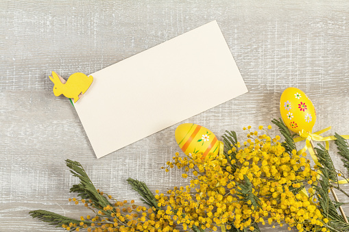 Easter accessories, mimosa and yellow daffodils on a light wooden surface.