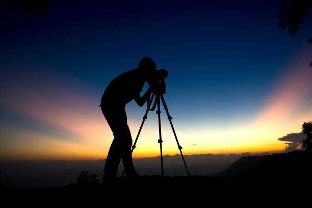 istock Silhouette Young Man Photographing While Standing On Mountain Against Sky During Sunset 938863560