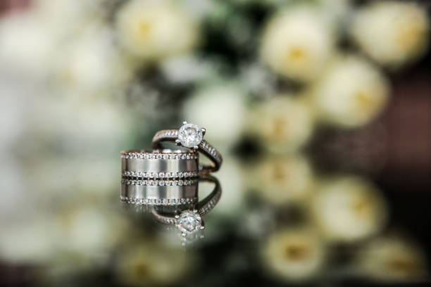 istock Wedding and engagement rings on the flowered glass background 938871112