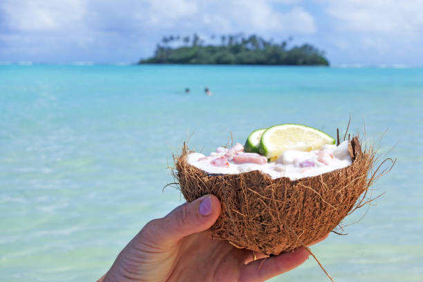 Woman holds Ceviche Dish served in a coconut shell against a islet in Muri lagoon Rarotonga Cook Islands stock photo