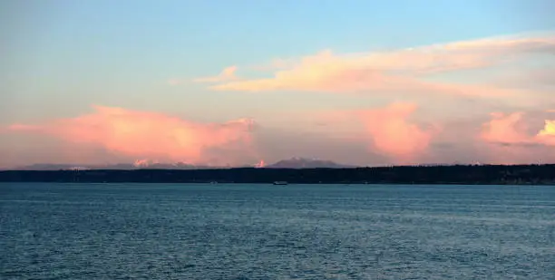 Puffy pink clouds look like spun sugar at sunset over Puget Sound, with Washington State Ferry visible in distance