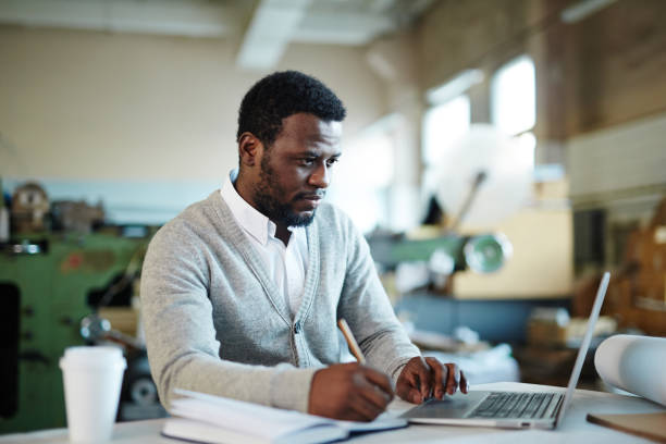 istock Concentrated African editor viewing online text before printing 938886892