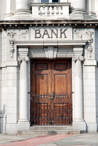 Classic antique old British bank door with sign engraved in stone or concrete above the door of the bank building, Classic columns and architectural features. Front view. Financial building. 