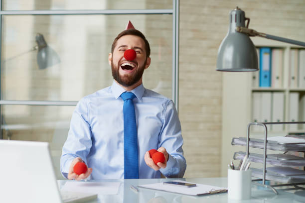Hilarious crazy bearded businessman in clowns nose preparing for juggling and laughing at himself in modern office