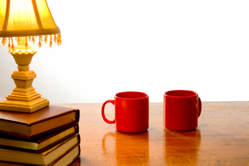 Two red coffee cups on a table by a little desk lamp.