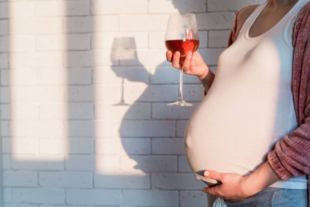 donna incinta con bicchiere di vino rosso in mano - abdomen addiction adult alcohol foto e immagini stock