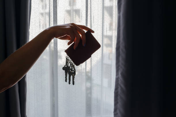 Asian female hand holding leather key holder with backlight and building behind curtains background