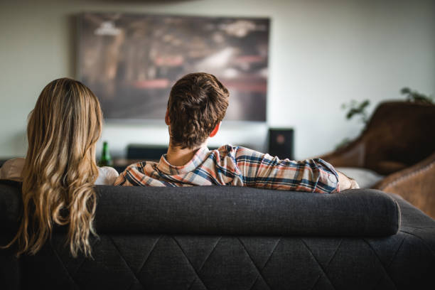 istock Back view of a couple watching TV on sofa at home. 938963512