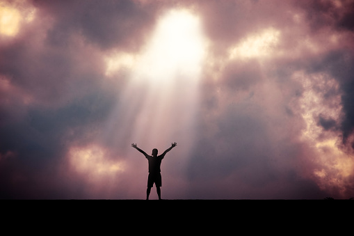Man holding arms up in praise to God against sunrise at morning with sky and vintage background.