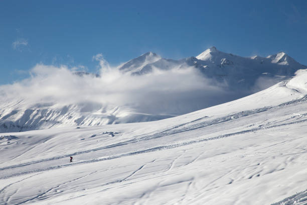 istock Skier performs downhill on the background of mountain peaks and clouds 938969212