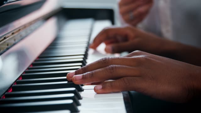 Close Up Of Pupil With Teacher Playing Piano In Music Lesson