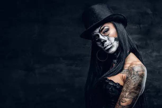 A girl in stylish top hat with skull make up and tattoo on arm. Halloween party.