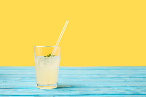 fresh cold summer drink in glass with drinking straw on turquoise wooden table top