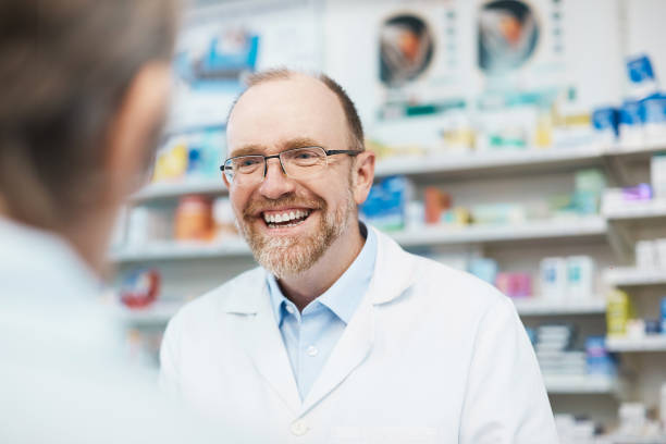 улыбающийся мужчина фармацевт приветствует клиента - pill bottle pharmacy medicine shelf стоковые фото и изображения