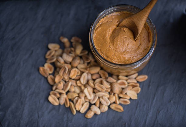 istock Bowl of peanut butter and peanuts on dark background from top view 938990944