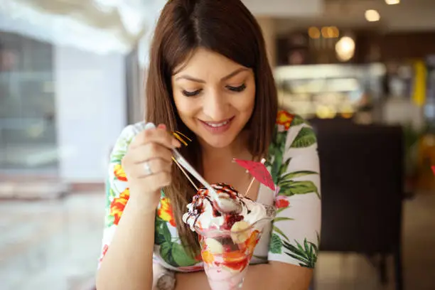 Young pregnant woman eating sundae in cafe