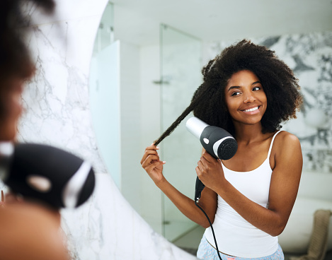 Shot of an attractive young woman blowdrying her hair at home