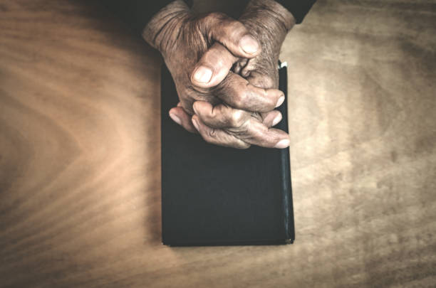 istock Old hands on the bible on a wood background. 939008856