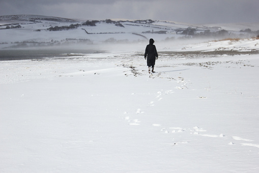 A lone person walking along the snow covered beach at Ettrick Bay, Isle of Bute, Scotland.
