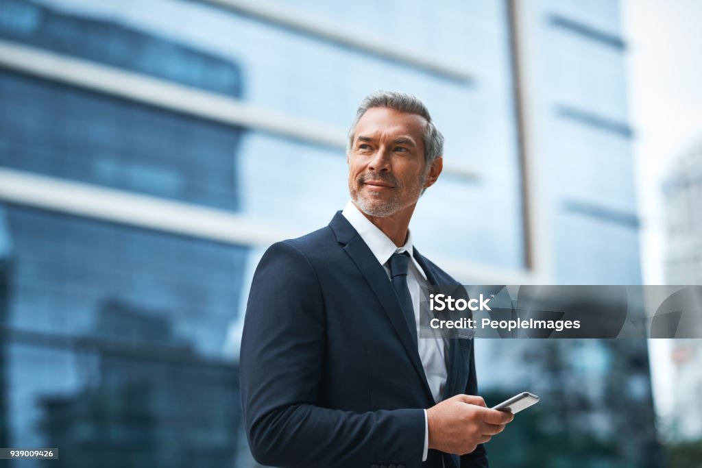 Hard work, determination, persistence creates a boss Shot of a handsome mature businessman in corporate attire using a cellphone outside outside during the day Businessman Stock Photo