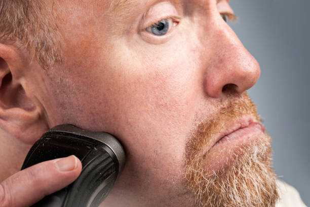 istock Bearded man grimaces as he shaves sideburns with electric razor 939018016