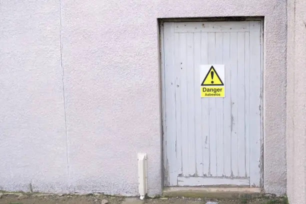 Asbestos danger warning sign on door old building safety hazard to lungs and breathing