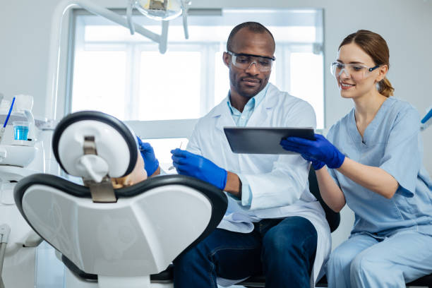 Young nurse showing email on tablet to dentist examining patient Important letter. Pleasant young female nurse showing an important email on tablet to the dentist carrying out the examination of an oral cavity of a little girl tablet pc and digital hospital tools stock pictures, royalty-free photos & images