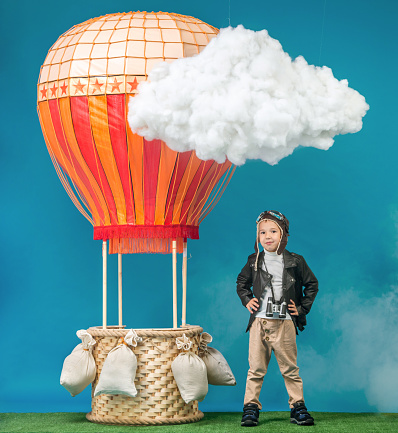 The happy boy dressed as vintage aeronauts clothes standing next to a hot-air balloon