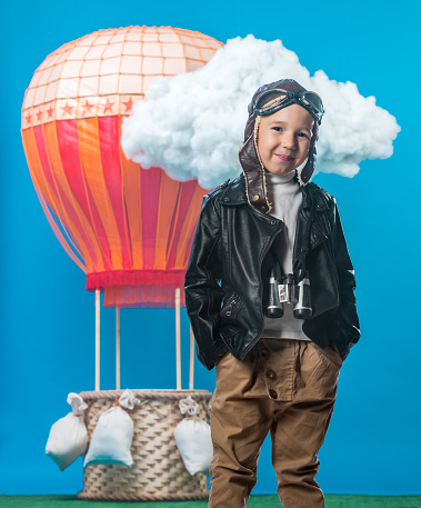The smiling boy dressed as vintage aeronaut is standing on a hot-air balloon background