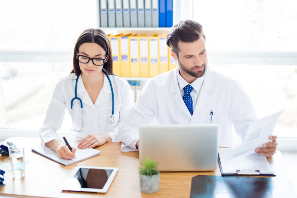 istock Two person: professional doctor and his assistant in glasses cooperate together by analyzing and writing diagnosis 939034222