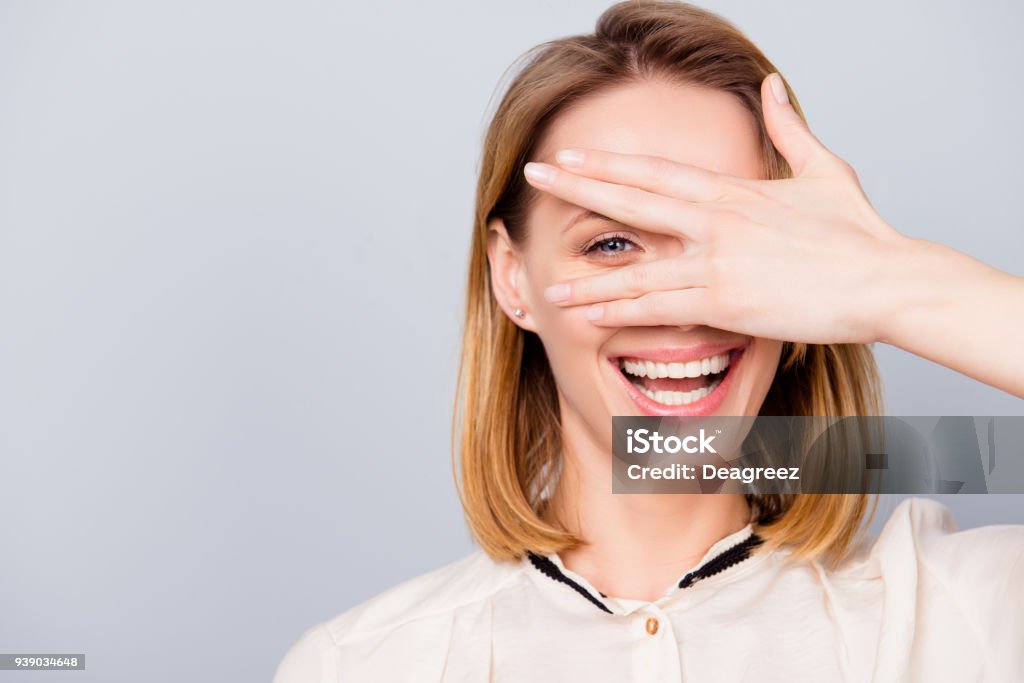 Blonde junge Frau mit strahlenden Lächeln ist durch ihre Hand suchen. Sie trägt casual-Outfit und steht auf grauem Hintergrund - Lizenzfrei Auge Stock-Foto
