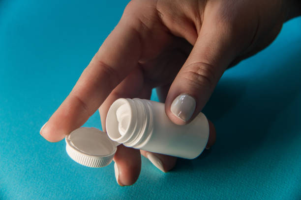 istock Womans hand opens White plastic medical container for pills isolated on green 939039164
