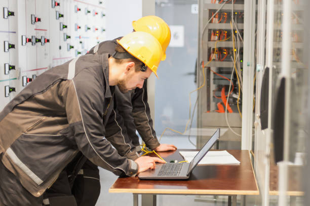 Two maintenance engineers inspect relay protection system with laptop comp Two maintenance engineers inspect relay protection system with laptop computer. Bay control unit. Medium voltage switchgear coupling stock pictures, royalty-free photos & images