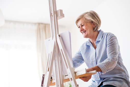 A happy senior woman painting at home.