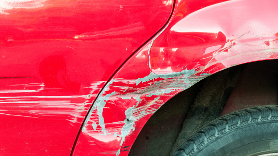 Red damaged car in crash accident with scratched paint and dented metal body