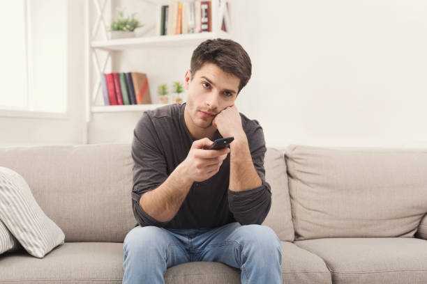 hombre joven aburrido viendo la televisión en casa - television boredom men sofa fotografías e imágenes de stock