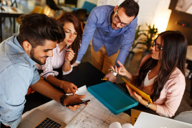 istock Group of designers working on new project .They using laptop and discuss about blueprints. 939054728