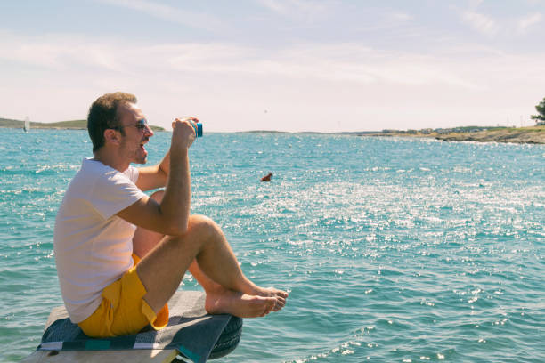 istock Tourist handsome man enjoying the view on the beach while using old retro camera. Summer concept. 939075802