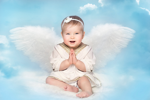 Angel Baby with Amur Wings, Kid Cupid Sitting on Blur Sky background, Happy Girl Child Portrait