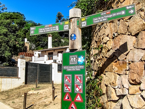 Lloret de Mar, Girona Province, Autonomous Community of Catalonia, Spain - October 7, 2013: Signpost for tourists on a pedestrian path on the precipitous Mediterranean coast between the resort towns of Lloret de Mar and Tossa de Mar on the Costa Brava