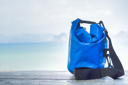 Blue waterproof bag on wooden table with blurry seascape background.
