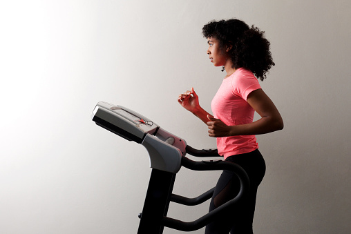 Side portrait of fit young woman running on treadmill indoors