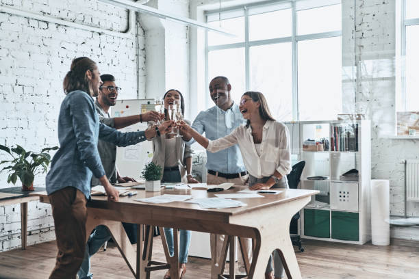 To our team! Group of happy business people toasting each other and smiling while standing in the board room office parties stock pictures, royalty-free photos & images